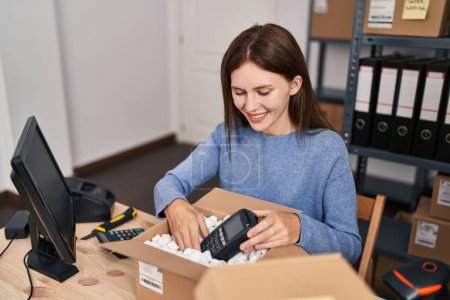 Téléchargez les photos : Jeune femme blonde commerce électronique travailleur d'affaires emballage téléphone de données sur la boîte en carton au bureau - en image libre de droit