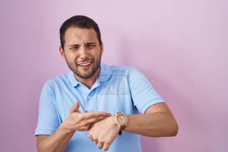 Téléchargez les photos : Homme hispanique debout sur fond rose à la hâte pointant pour regarder le temps, l'impatience, bouleversé et en colère pour retard de délai - en image libre de droit