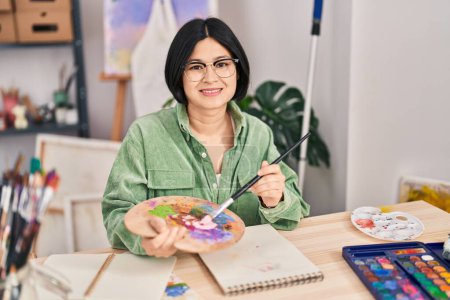 Téléchargez les photos : Jeune artiste chinoise souriante dessin confiant sur carnet au studio d'art - en image libre de droit