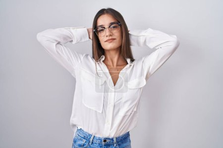 Téléchargez les photos : Jeune femme brune portant des lunettes de détente et d'étirement, bras et mains derrière la tête et le cou souriant heureux - en image libre de droit
