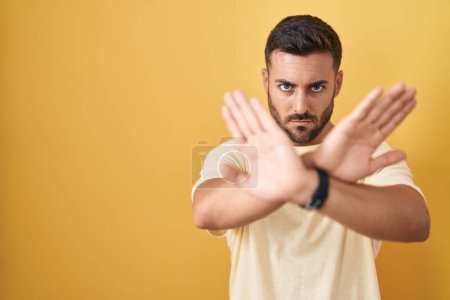 Téléchargez les photos : Bel homme hispanique debout sur fond jaune expression de rejet traversant les bras et les paumes faisant signe négatif, visage en colère - en image libre de droit