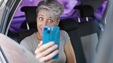 Téléchargez les photos : Jeune femme passager assis sur la voiture ayant appel vidéo à la rue - en image libre de droit