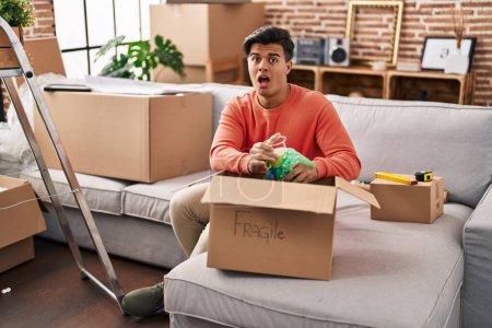 Photo for Hispanic man moving to a new home unpacking in shock face, looking skeptical and sarcastic, surprised with open mouth - Royalty Free Image