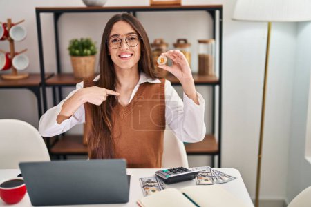 Photo for Young brunette woman working with laptop holding virtual currency bitcoin pointing finger to one self smiling happy and proud - Royalty Free Image