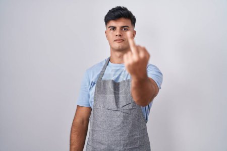 Foto de Hispanic young man wearing apron over white background showing middle finger, impolite and rude fuck off expression - Imagen libre de derechos