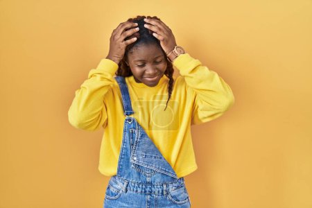 Photo for African woman standing over yellow background suffering from headache desperate and stressed because pain and migraine. hands on head. - Royalty Free Image
