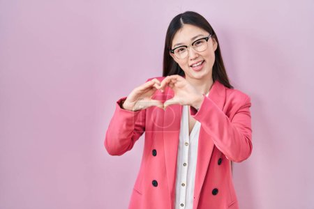 Foto de Chino negocio joven mujer con gafas sonriendo en el amor haciendo corazón símbolo de forma con las manos. concepto romántico. - Imagen libre de derechos