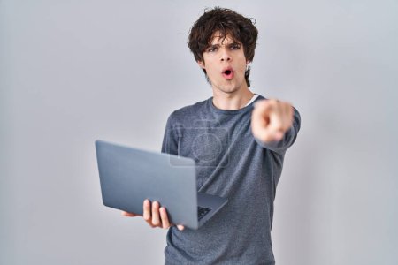 Téléchargez les photos : Jeune homme travaillant à l'aide d'un ordinateur portable pointant du doigt la caméra et à vous, geste confiant regardant sérieux - en image libre de droit