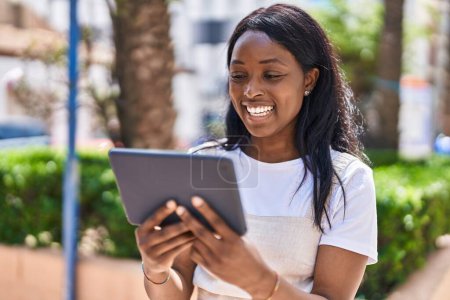 Téléchargez les photos : Jeune femme afro-américaine souriante confiante regarder la vidéo sur touchpad au parc - en image libre de droit