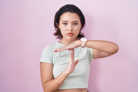 Photo for Hispanic young woman standing over pink background doing time out gesture with hands, frustrated and serious face - Royalty Free Image