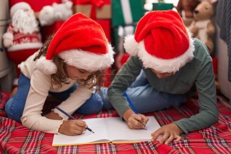 Photo for Two kids writing on notebook sitting on floor by christmas tree at home - Royalty Free Image