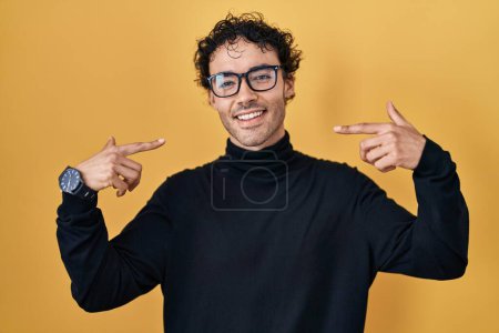 Téléchargez les photos : Hispanic man standing over yellow background smiling cheerful showing and pointing with fingers teeth and mouth. dental health concept. - en image libre de droit
