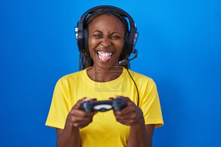 Foto de Afro americana mujer jugando video juegos palanca lengua fuera feliz con divertido expresión. - Imagen libre de derechos