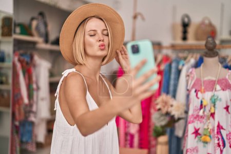 Téléchargez les photos : Jeune femme blonde client faire selfie par smartphone embrasser au magasin de vêtements - en image libre de droit