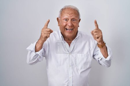 Foto de Senior man with grey hair standing over isolated background smiling amazed and surprised and pointing up with fingers and raised arms. - Imagen libre de derechos