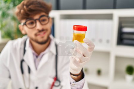 Téléchargez les photos : Jeune homme arabe portant un uniforme de médecin tenant une éprouvette d'urine à la clinique - en image libre de droit