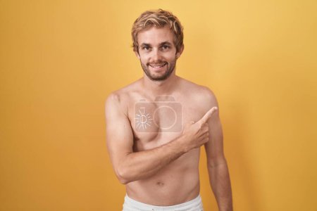 Photo for Caucasian man standing shirtless wearing sun screen cheerful with a smile on face pointing with hand and finger up to the side with happy and natural expression - Royalty Free Image