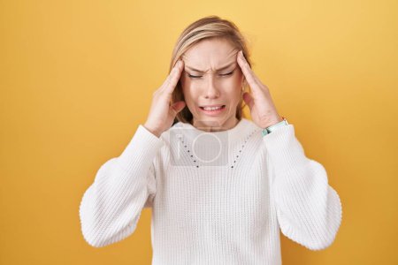 Photo for Young caucasian woman wearing white sweater over yellow background with hand on head, headache because stress. suffering migraine. - Royalty Free Image