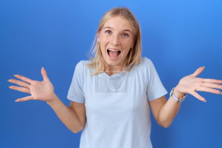 Foto de Mujer caucásica joven vistiendo casual camiseta azul celebrando loco y sorprendido por el éxito con los brazos levantados y los ojos abiertos gritando emocionado. concepto ganador - Imagen libre de derechos