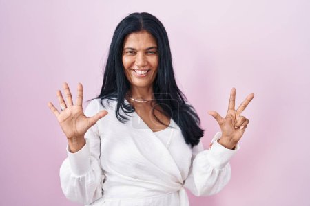Photo for Mature hispanic woman standing over pink background showing and pointing up with fingers number eight while smiling confident and happy. - Royalty Free Image