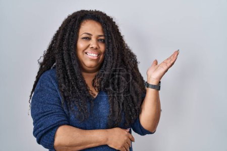 Photo for Plus size hispanic woman standing over white background smiling cheerful presenting and pointing with palm of hand looking at the camera. - Royalty Free Image