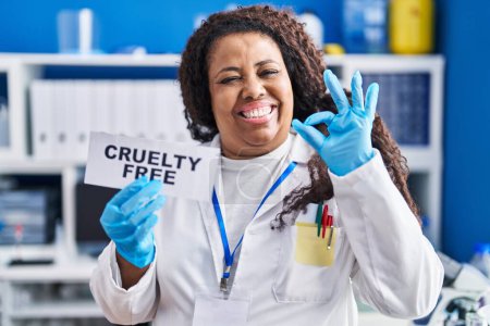 Foto de Más tamaño hispana mujer trabajando en laboratorio libre de crueldad haciendo ok signo con los dedos, sonriendo gesto amistoso excelente símbolo - Imagen libre de derechos