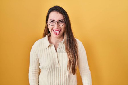 Photo for Young hispanic woman standing over yellow background sticking tongue out happy with funny expression. emotion concept. - Royalty Free Image