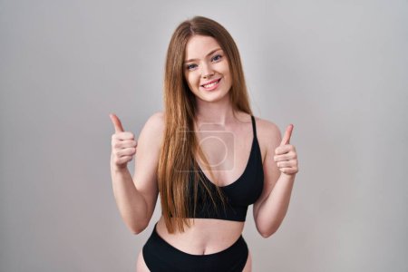 Photo for Young caucasian woman wearing lingerie success sign doing positive gesture with hand, thumbs up smiling and happy. cheerful expression and winner gesture. - Royalty Free Image