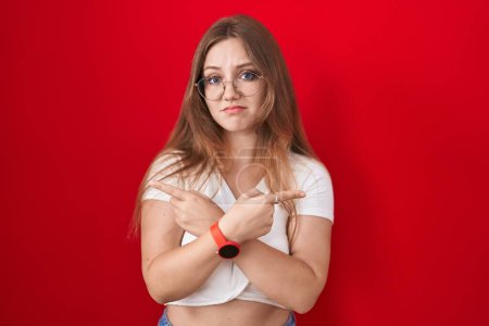 Photo for Young caucasian woman standing over red background pointing to both sides with fingers, different direction disagree - Royalty Free Image