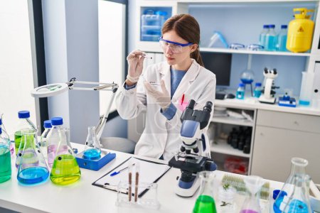 Téléchargez les photos : Jeune femme blonde scientifique tenant un échantillon avec une pince à épiler au laboratoire - en image libre de droit