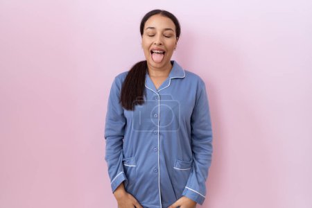 Photo for Young arab woman wearing blue pajama sticking tongue out happy with funny expression. emotion concept. - Royalty Free Image