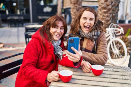 Téléchargez les photos : Deux femmes mère et fille en utilisant smartphone boire du café à la terrasse du café - en image libre de droit