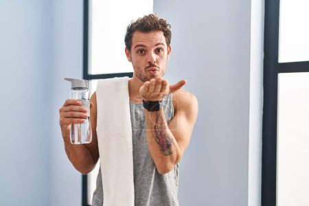 Photo for Young hispanic man wearing sportswear drinking water looking at the camera blowing a kiss with hand on air being lovely and sexy. love expression. - Royalty Free Image