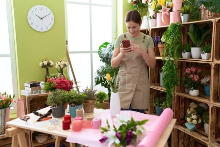 Téléchargez les photos : Jeune belle fleuriste femme faire une photo pour fleurir par smartphone à la boutique de fleurs - en image libre de droit