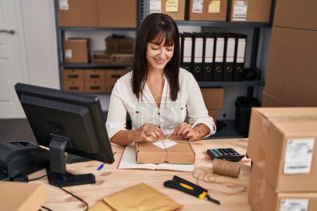 Photo for Young beautiful hispanic woman ecommerce business worker smiling confident preparing package at office - Royalty Free Image