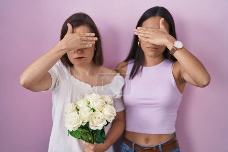 Téléchargez les photos : Mère et fille hispaniques tenant bouquet de fleurs blanches couvrant les yeux avec la main, l'air grave et triste. concept de non-visibilité, de dissimulation et de rejet - en image libre de droit
