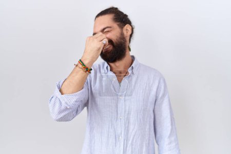 Téléchargez les photos : Homme hispanique avec barbe portant une chemise décontractée sentant quelque chose de puant et dégoûtant, odeur intolérable, retenant souffle avec les doigts sur le nez. mauvaise odeur - en image libre de droit