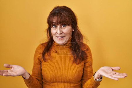 Photo for Middle age hispanic woman standing over yellow background clueless and confused with open arms, no idea concept. - Royalty Free Image