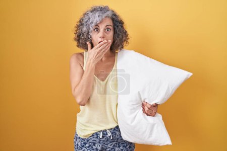 Photo for Middle age woman with grey hair wearing pijama hugging pillow shocked covering mouth with hands for mistake. secret concept. - Royalty Free Image