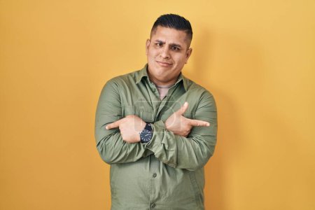 Téléchargez les photos : Jeune homme hispanique debout sur fond jaune pointant des deux côtés avec les doigts, direction différente en désaccord - en image libre de droit