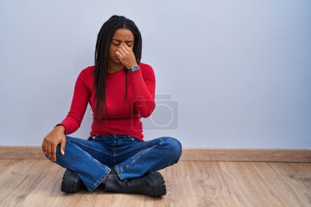 Photo for Young african american with braids sitting on the floor at home tired rubbing nose and eyes feeling fatigue and headache. stress and frustration concept. - Royalty Free Image