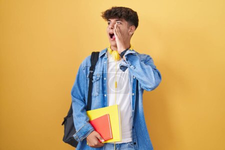 Photo for Hispanic teenager wearing student backpack and holding books shouting and screaming loud to side with hand on mouth. communication concept. - Royalty Free Image