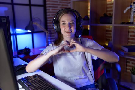 Foto de Joven mujer caucásica streamer sonriendo confiado haciendo símbolo del corazón con las manos en la sala de juegos - Imagen libre de derechos