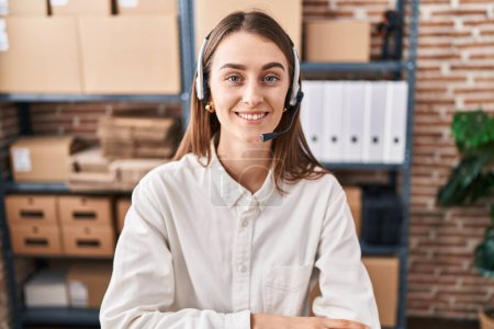 Téléchargez les photos : Jeune femme caucasienne travaillant dans une petite entreprise e-commerce portant casque regardant positif et heureux debout et souriant avec un sourire confiant montrant des dents - en image libre de droit