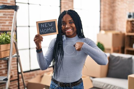 Photo for African american woman holding blackboard with new home text pointing finger to one self smiling happy and proud - Royalty Free Image