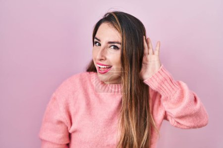 Photo for Young hispanic woman standing over pink background smiling with hand over ear listening an hearing to rumor or gossip. deafness concept. - Royalty Free Image