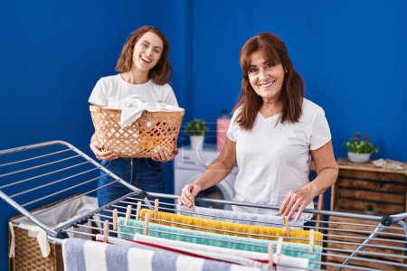 Photo for Two women mother and daughter hanging clothes on clothesline at laundry room - Royalty Free Image