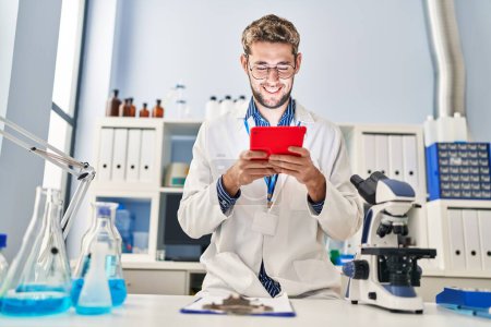 Photo for Young man scientist smiling confident using touchpad at laboratory - Royalty Free Image