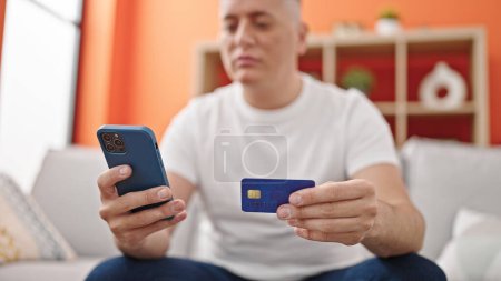 Foto de Joven caucásico hombre de compras con teléfono inteligente y tarjeta de crédito sentado en el sofá en casa - Imagen libre de derechos
