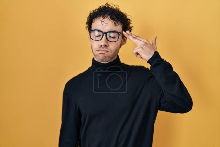 Foto de Hispanic man standing over yellow background shooting and killing oneself pointing hand and fingers to head like gun, suicide gesture. - Imagen libre de derechos
